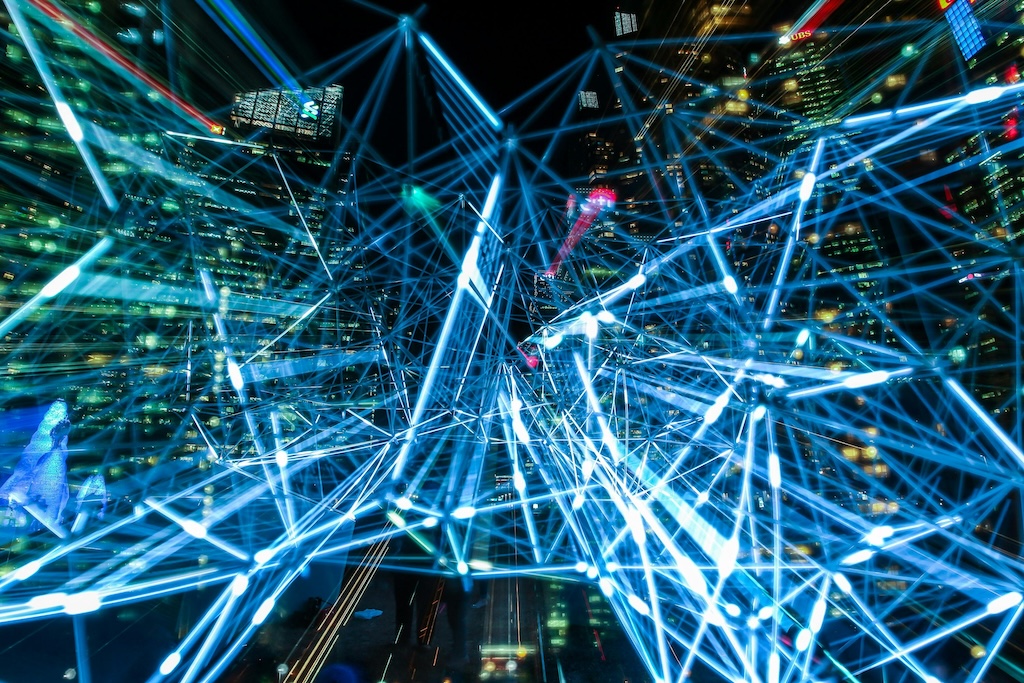Network of illuminated blue lines connecting buildings in a nighttime cityscape.